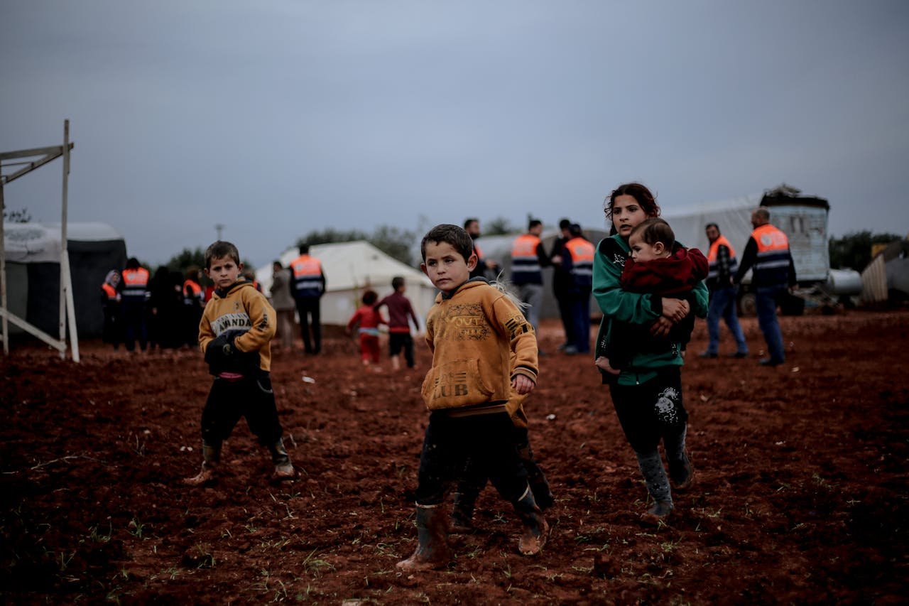 Offerings Children navigating a muddy field in Idlib, Syria, showing resilience amidst adversity.